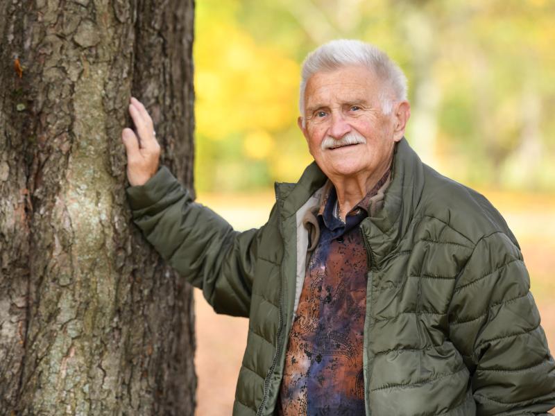 Ein älterer Mann lehnt seine Hand an einen Baum.