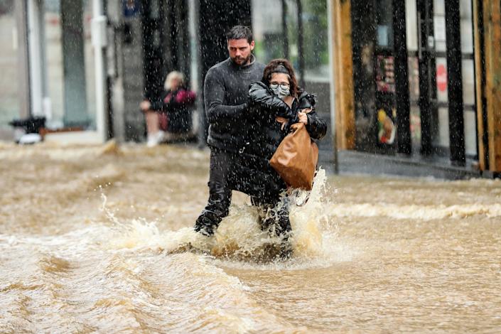 Ein Mann hilft einer Frau am Donnerstag, eine überflutete Straße in der Innenstadt von Spa, Belgien, zu navigieren