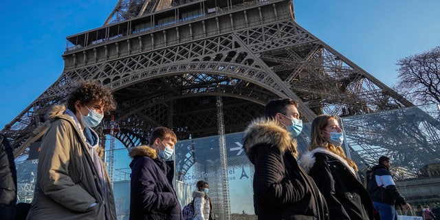 Menschen, die Gesichtsmasken tragen, um sich vor COVID-19 zu schützen, gehen am Dienstag, 21. Dezember 2021, am Eiffelturm in Paris vorbei (AP Photo / Michel Euler)